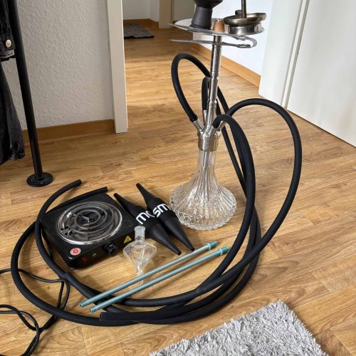 Shisha mit Glasbowl, Schlauch und Heizplatte auf Holzboden.