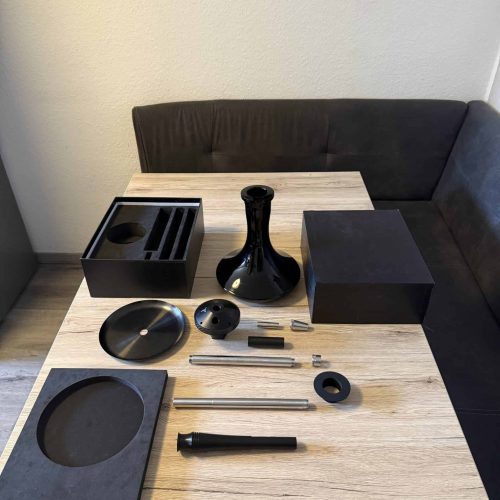 Schwarzes Shisha-Set mit Zubehör auf einem Holztisch, bereit zum Aufbau.