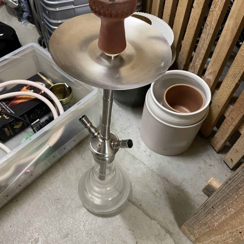 Shisha mit Tonkopf und Metallaufsatz, bereit zum Rauchen in einem Lagerraum.