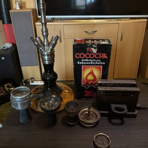 Komplettes Shisha-Set mit Kohle, Tabak und Zubehör auf Tisch.