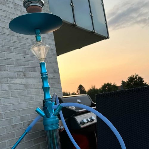 Shisha mit blauer Glasbasis und Silikonschlauch auf Balkon im Sonnenuntergang.