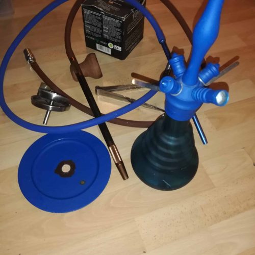 Shisha mit Rauchsäule, Schlauch und Zubehör auf Holztisch.