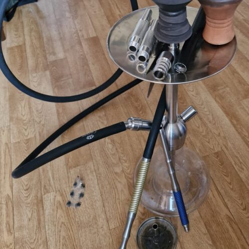 Rauchsäule mit verschiedenen Shisha-Teilen und Zubehör auf einem Tisch.