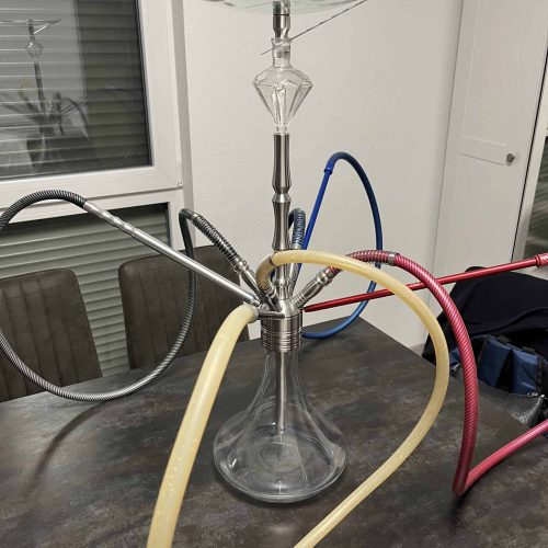 Shisha-Kopf mit Glasbowl, Schläuchen und Metallstange auf Tisch.
