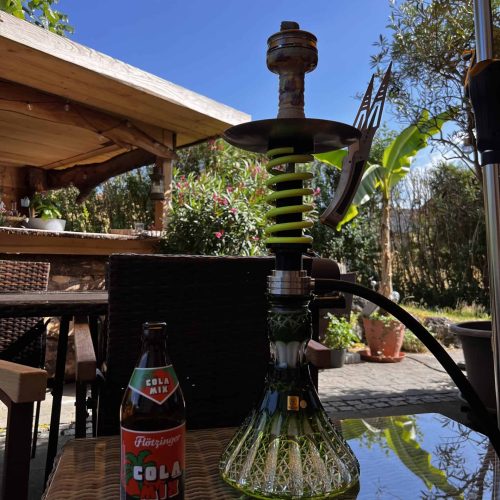 Rauchsäule mit Wasserpfeife auf einem Tisch im Garten unter einem Sonnenschirm.