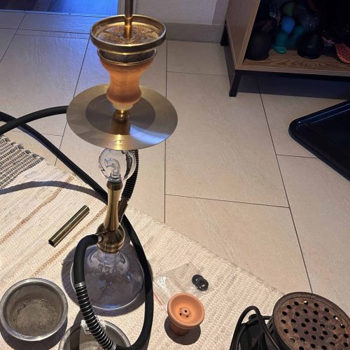 Shisha mit Glasbowl, Schlauch und Zubehör auf Boden.