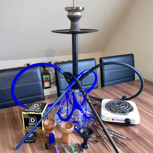 Shisha mit Glaskörper, Schlauch und Zubehör auf Tisch.