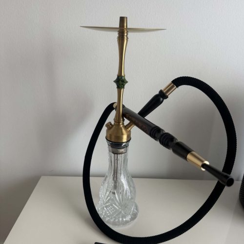 Shisha mit Glasbowl, Schlauch und Metallhaken auf weißem Tisch.