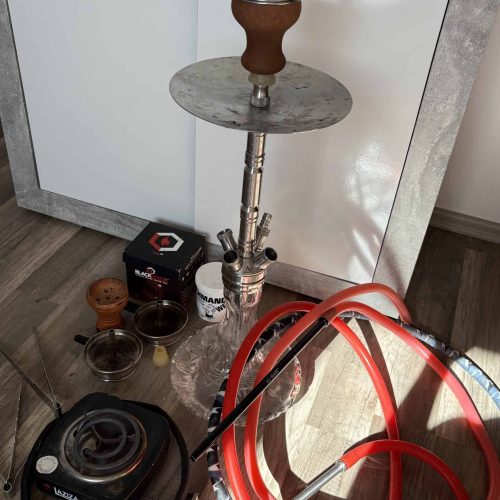 Shisha mit Glasbowl, Schlauch und Heizplatte auf Boden.