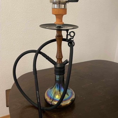 Shisha mit Glasbowl, Silikonschlauch und Metallzubehör auf Tisch.