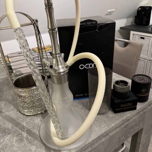 Rauchende Wasserpfeife mit Silikonschlauch und Zubehör auf Tisch.