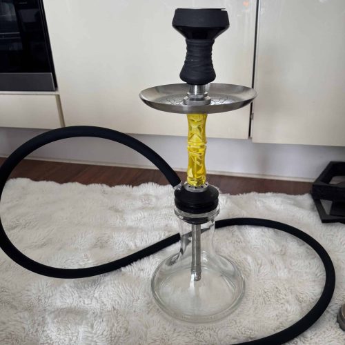 Shisha mit Glas-Schüssel, Silikonschlauch und Metallzubehör, auf Teppichboden im Raum.