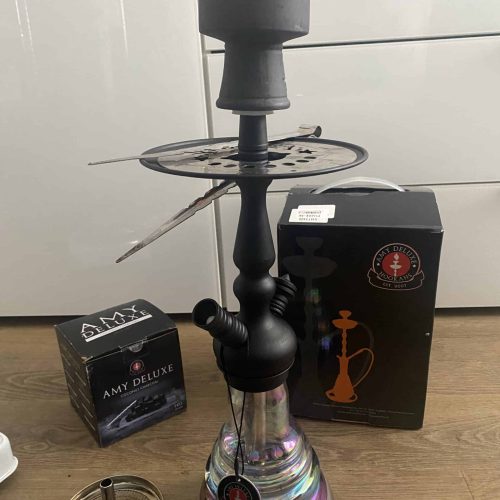 Shisha mit Glaskolben, Rauchsäule und Zubehör, auf Holztisch.