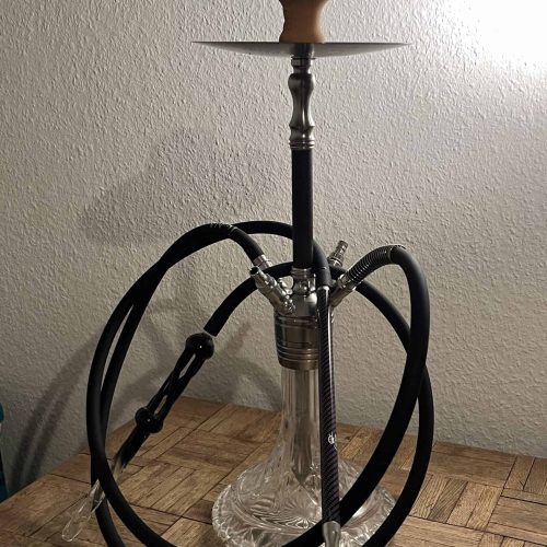 Shisha mit Glasgefäß, Kopf und Schläuchen, auf Holztisch.