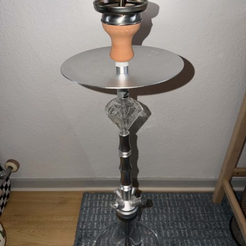 Shisha-Hookah mit Glasbowl und Metallstücken, auf Boden stehend.