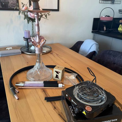 Rauchsäule und Shisha-Zubehör auf einem Holztisch im Raum.