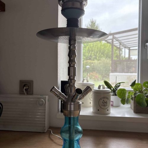 Rauchsäule mit Shisha auf einem Tisch, Blick nach draußen durch das Fenster, grüne Pflanzen im Hinte.