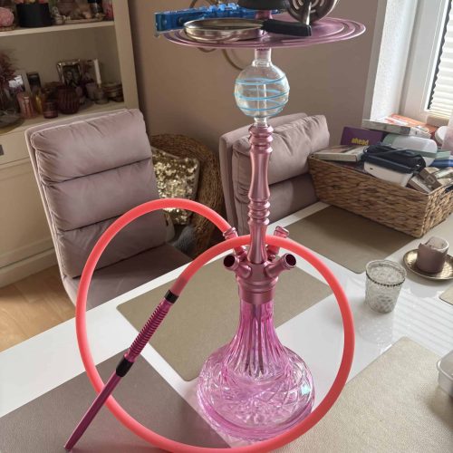 Pinke Shisha mit Glasbasis und Zubehör auf Esstisch im Wohnzimmer.