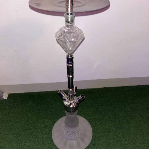Wasserpfeife mit Glas-Design und Metallaufsatz, auf grünem Teppich stehend.