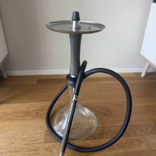 Shisha mit Glasbowl, Metallstange und Silikonschlauch auf Holztisch.