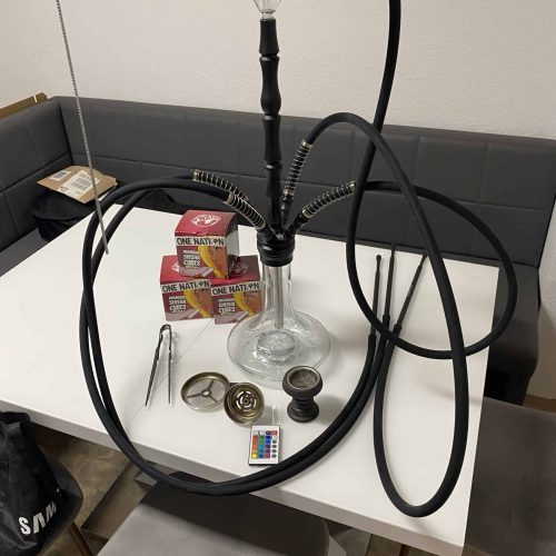 Shisha-Set mit Glasbowl, Schläuchen und Zubehör auf Tisch.