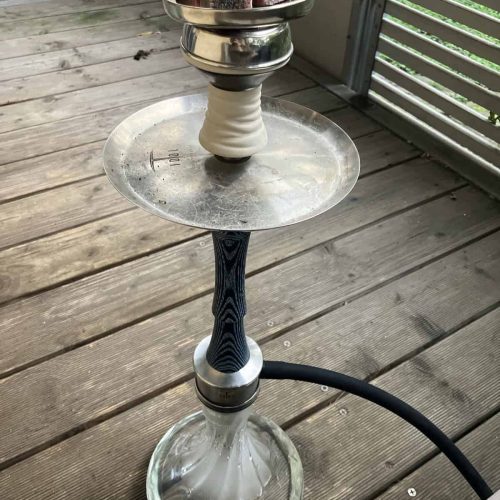 Shisha mit Glasbowl, Kohle und Schlauch auf Holzterrasse.
