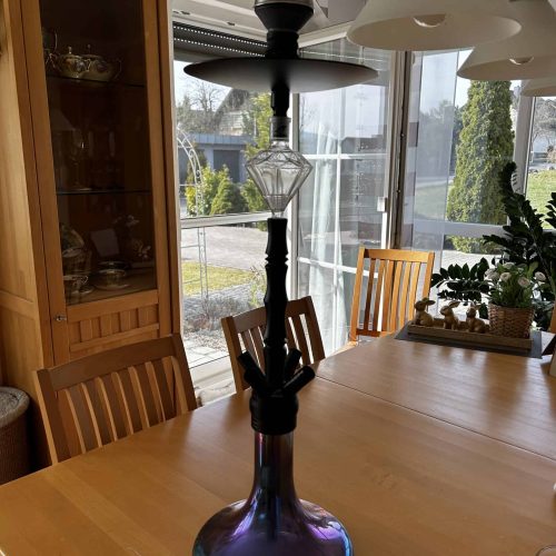 Dekorative Shisha auf Holztisch, gut beleuchteter Raum mit Pflanzen.