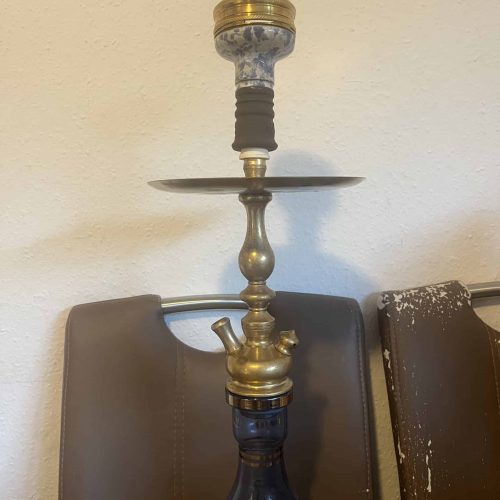 Alte Shisha mit Keramik-Kopf und Metall-Basis, auf einem Tisch stehend.