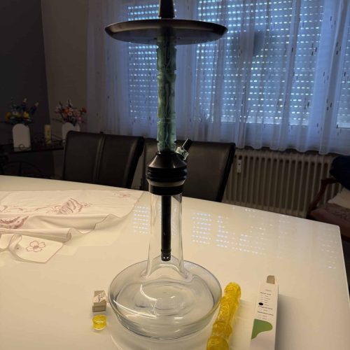 Shisha-Kopf mit Glasbowl auf Esstisch, Zubehör und Verpackung sichtbar.