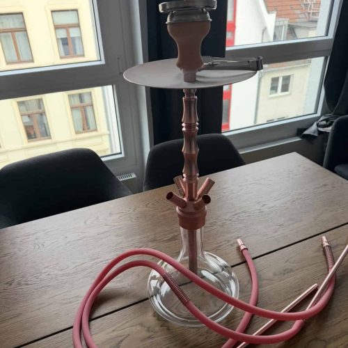 Shisha mit Glasbasis, Schlauch und Kopf auf Tisch.