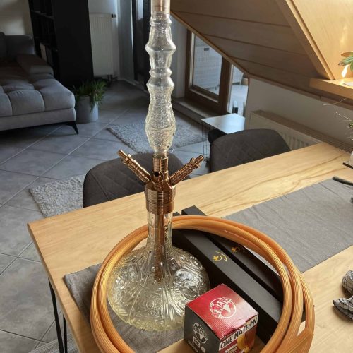 Shisha mit Glasbowl, Schlauch und Tabak auf Tisch.