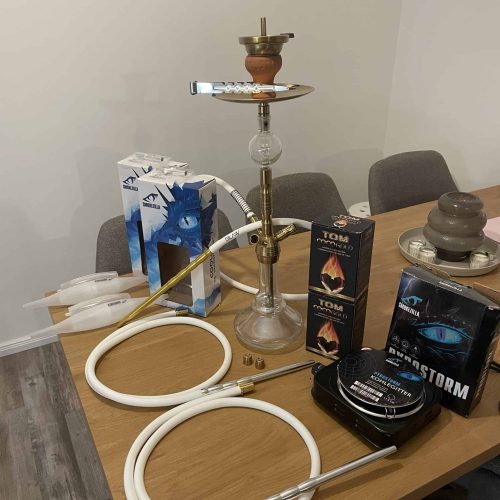 Shisha mit Rauchsäule, Tabak und Zubehör auf Tisch.