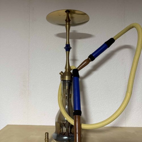 Shisha mit goldener Basis, blauer Düse und gelber Schlauch, auf Tisch stehend.