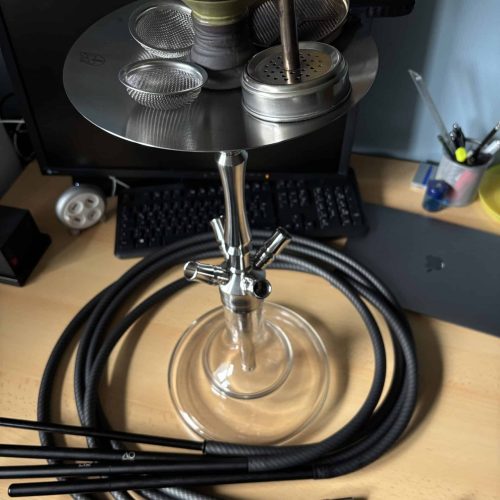 Shisha mit Glasbowl, Metallaufsatz und Schlauch auf Schreibtisch.