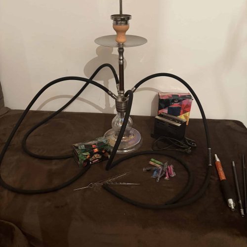 Shisha mit Rauchsäule, Schläuchen und Zubehör auf Tisch.