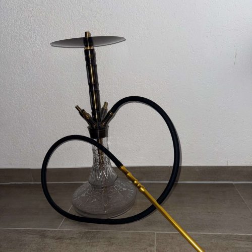 Shisha mit Glasbasis und goldener Tauchrohr, auf Boden stehend.