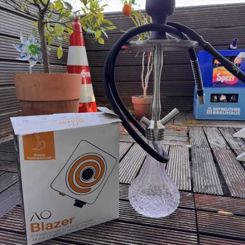 Shisha-Kohleanzünder mit Glasbowl auf Holzterrasse im Freien.