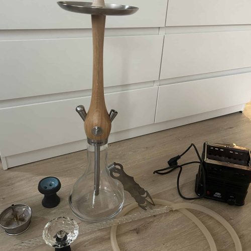 Rauchsäule mit Zubehör, inklusive Schlauch und Dichtungen, auf Holzboden vor weißem Schrank.