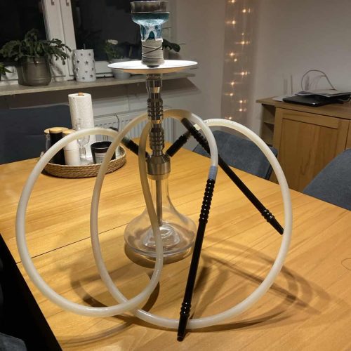 Wasserpfeife mit mehreren Schläuchen auf Holztisch, gemütliche Atmosphäre.
