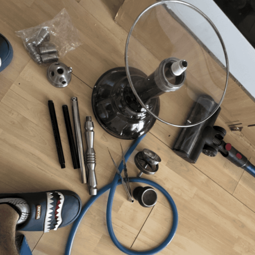 Shisha-Glasbowl und Metallteile auf Holzoberfläche.