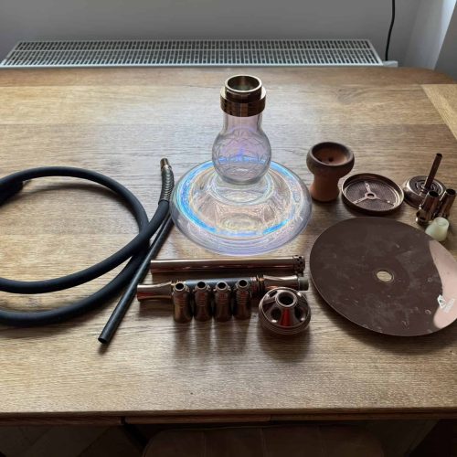 Shisha-Zubehör mit Glasbowl, Schlauch und Keramikteilen auf Holz.