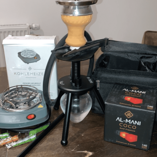 Shisha mit Heizgerät, Kohle und Zubehör auf Tisch.