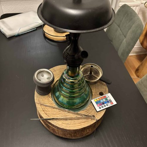 Shisha mit schwarzem Kopf und buntem Glasboden auf Tisch.