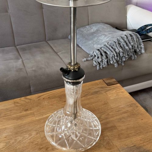 Moderne Glas-Shisha mit Metallaufsatz auf Holztisch.