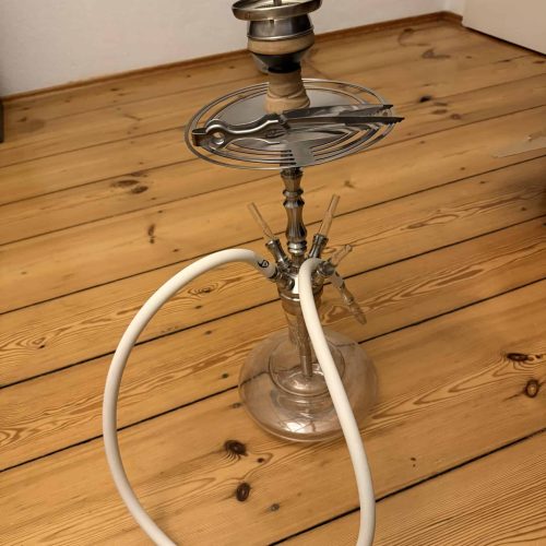 Alte Shisha mit Glasbowl und Metallteilen auf Holzboden.