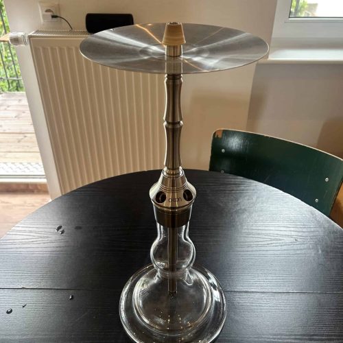 Hookah mit Metallplatte auf Glasbasis, auf Tisch in Innenraum.
