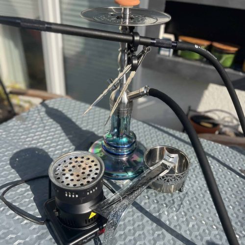 Rauchsäule mit Shisha, Heizgerät und Zubehör auf Tisch im Freien.
