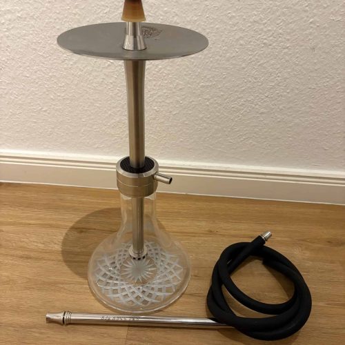 Shisha mit Glasbowl, Metallstange und Schlauch auf Holzboden.