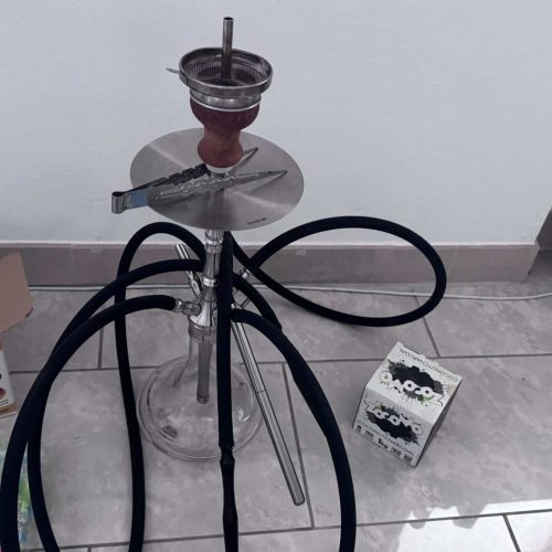 Shisha mit Glasbowl, Schlauch und Zubehör auf Fliesenboden.