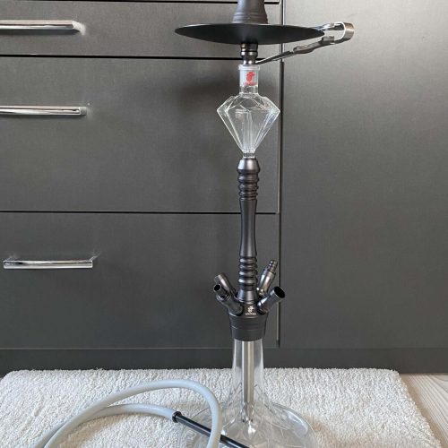 Moderne Shisha mit Glasbowl und Zubehör, auf Teppich vor grauer Schublade.
